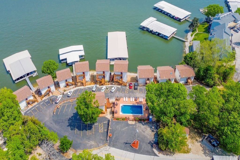 Vista aérea de una propiedad frente al agua con varias construcciones, una piscina y un estacionamiento.