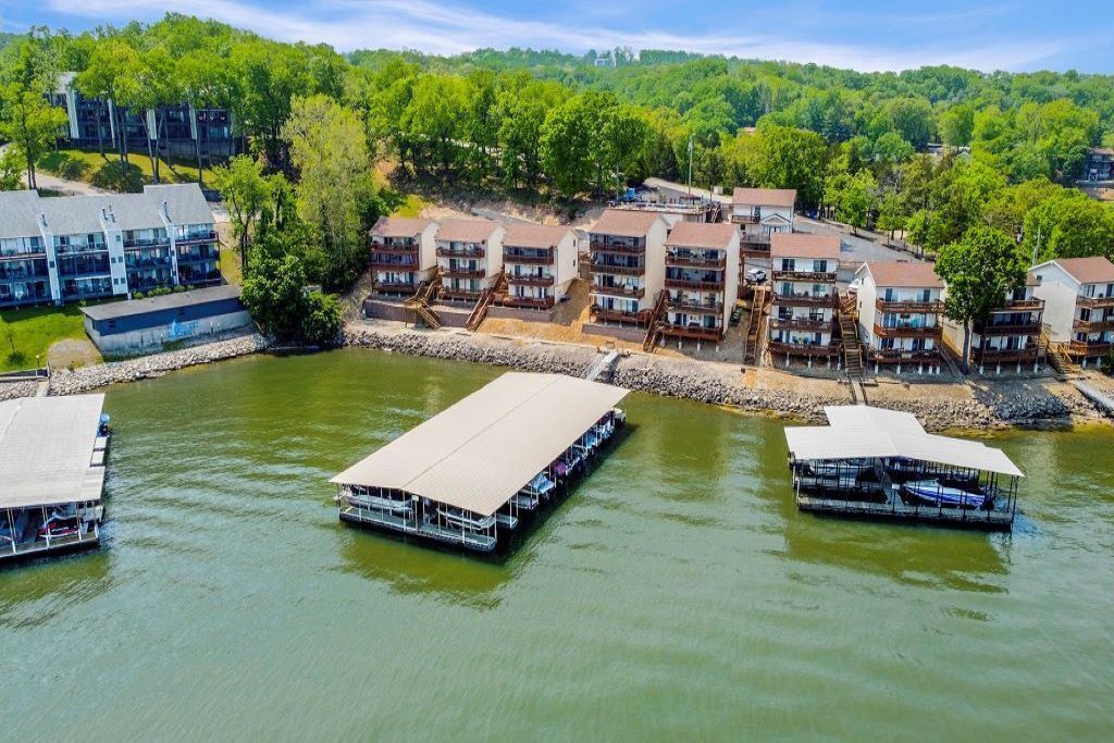 A riverside hotel with multiple buildings, docked boats, and a forested hillside.