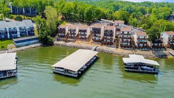 A riverside hotel with multiple buildings, docked boats, and a forested hillside.