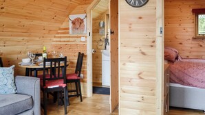 A wooden cabin interior with a dining area, a bed, and a large wall clock.
