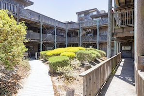 A multi-story wooden building with balconies, a wooden walkway, and a landscaped garden area.