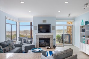 A living room with a fireplace, large windows, and a television. - Pelican 54: Relax with an ocean view. (Pajaro Dunes)