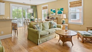 A spacious living room with a green sofa, a round coffee table, and a dining area with chairs. - Spa Villa home N Beach resort &spa 2 min to beach 7 pools attractions allow pet (North Myrtle Beach)