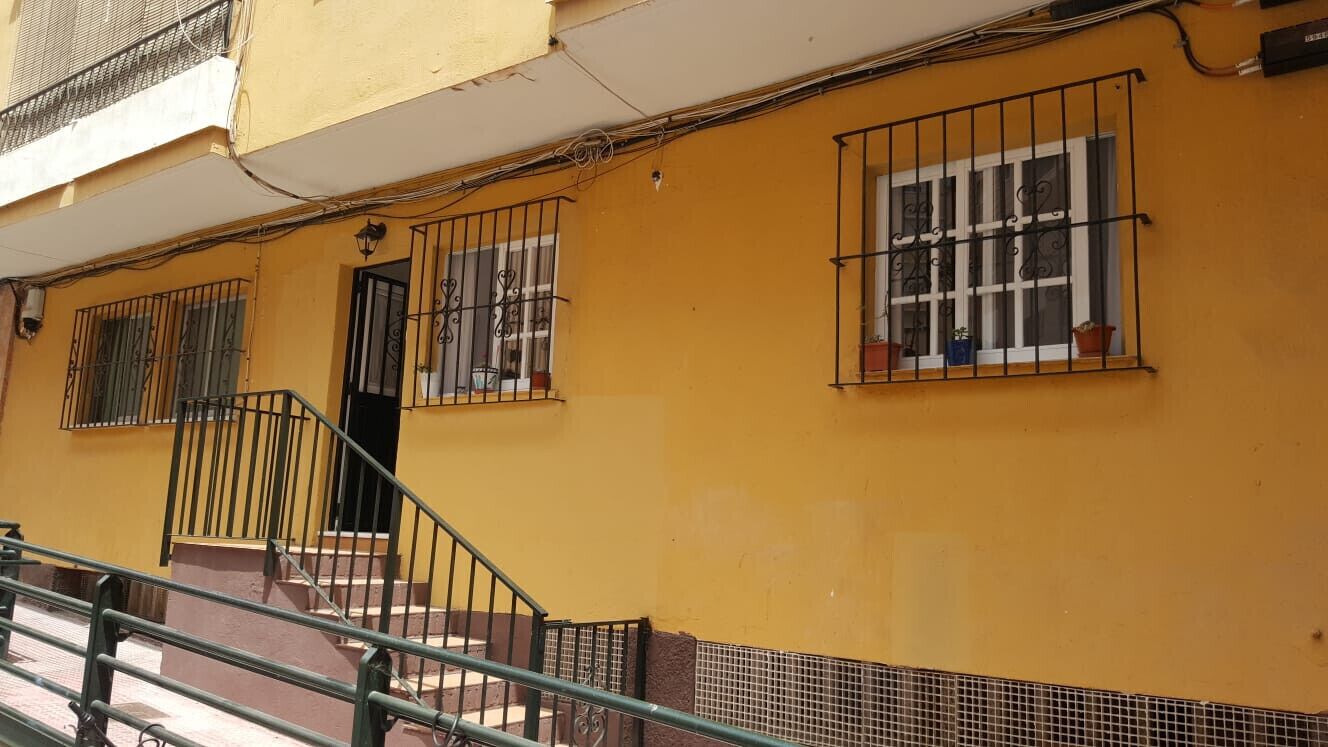 A yellow building with barred windows, a staircase, and a metal railing.