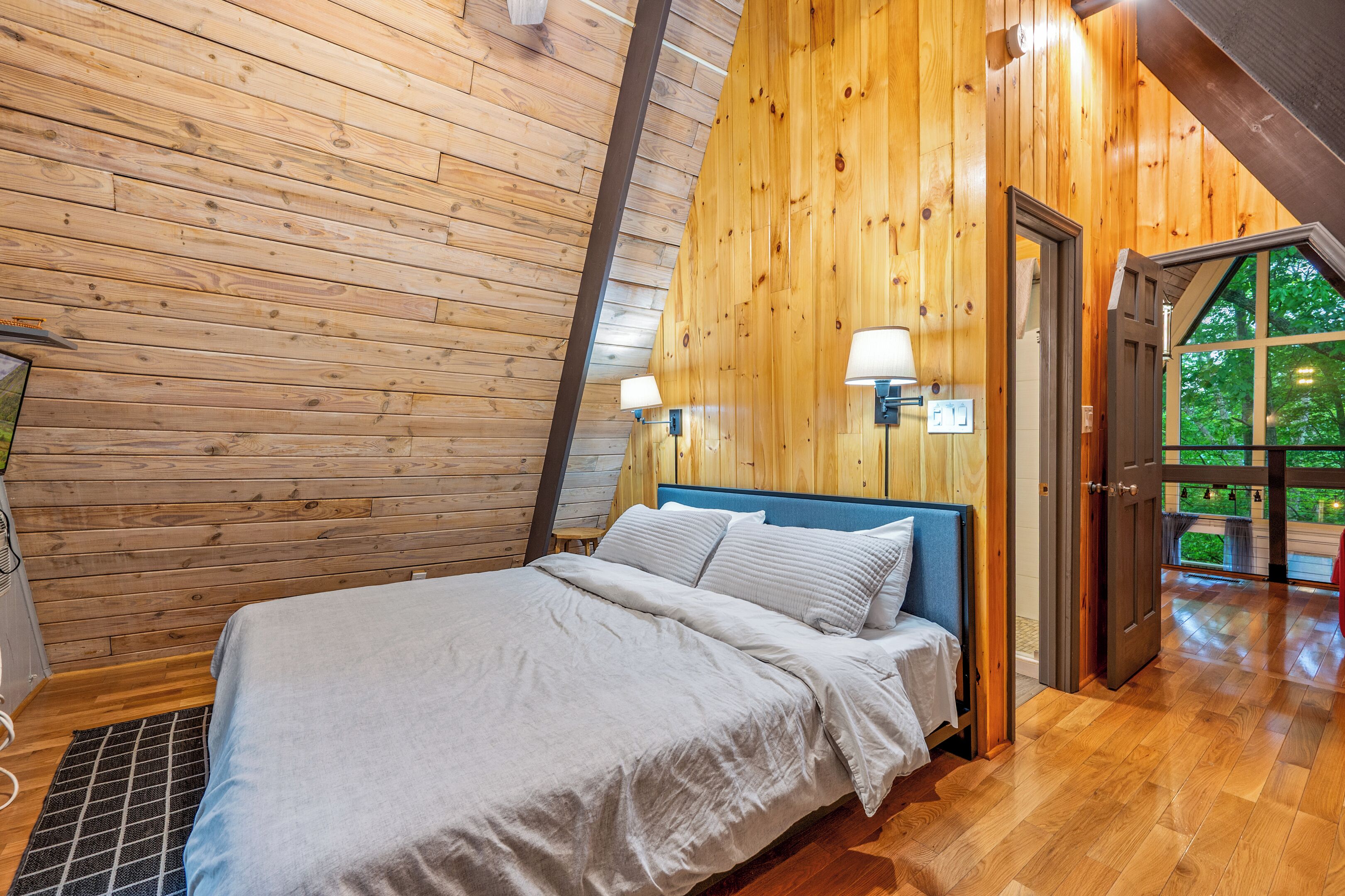 Ein Schlafzimmer mit Holzwänden, einem Bett, zwei Wandleuchten und einer Tür zu einem Außenbereich.