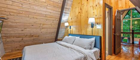 Ein Schlafzimmer mit Holzwänden, einem Bett, zwei Wandleuchten und einer Tür zu einem Außenbereich.
