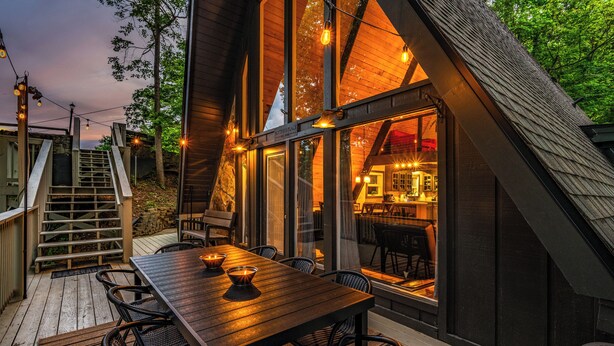 A wooden deck with a table and chairs, a staircase, and a view of the interior through large windows.