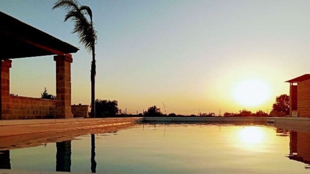 A calm outdoor pool area with a sunset in the background, surrounded by stone structures. - Villa Rakorishia Vu~ira rakorishia (Puglia)