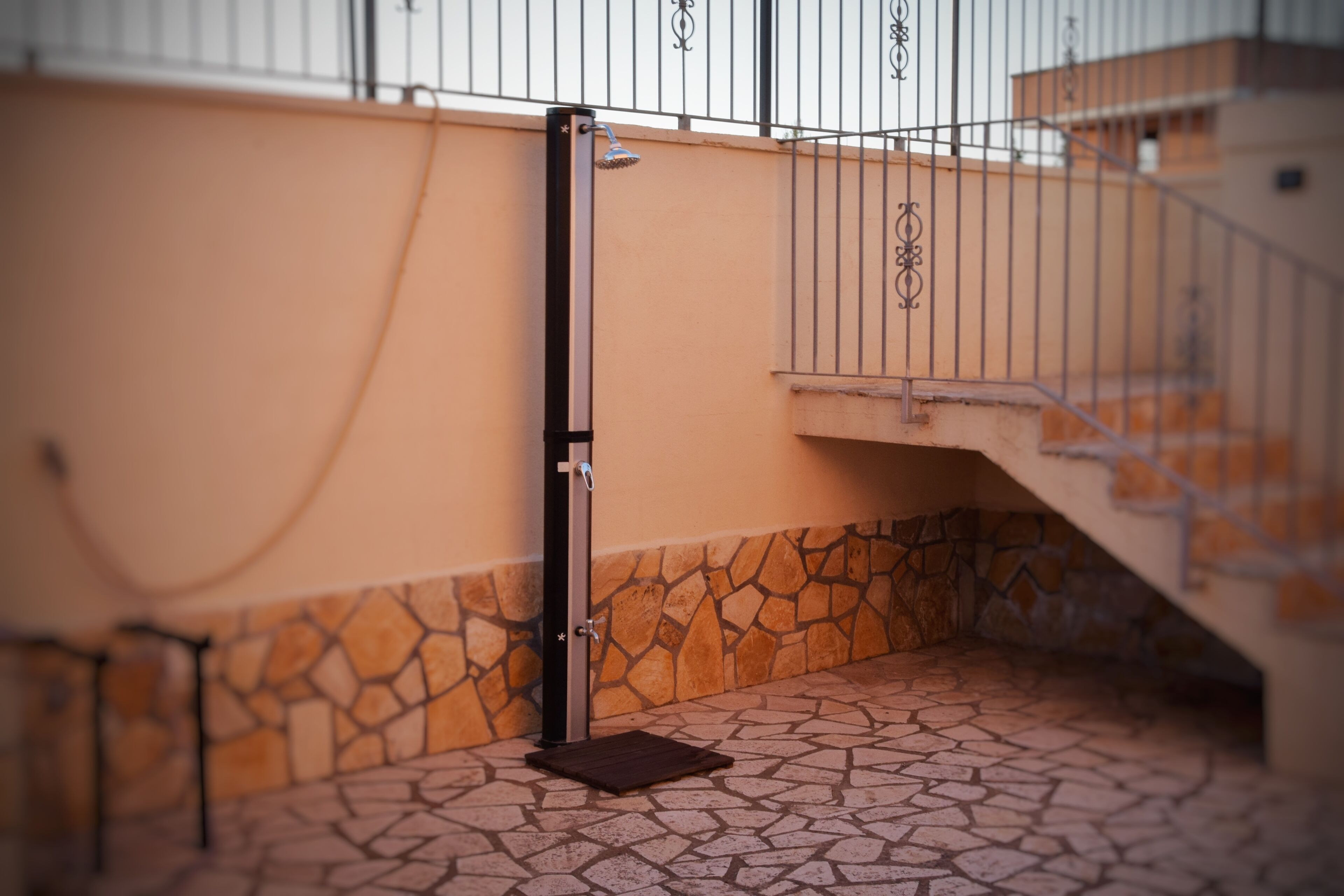 Un espace extérieur abrité, doté d’un sol carrelé en pierre, d’une rambarde en métal et d’une porte donnant accès à un escalier.