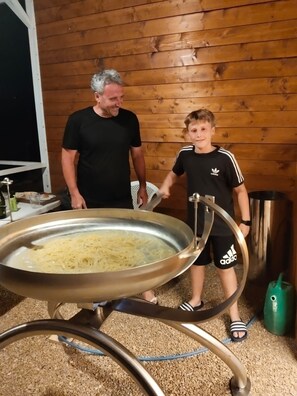 Un hombre y un niño en una habitación con paredes de madera, un cuenco metálico de comida y un bote verde de basura.