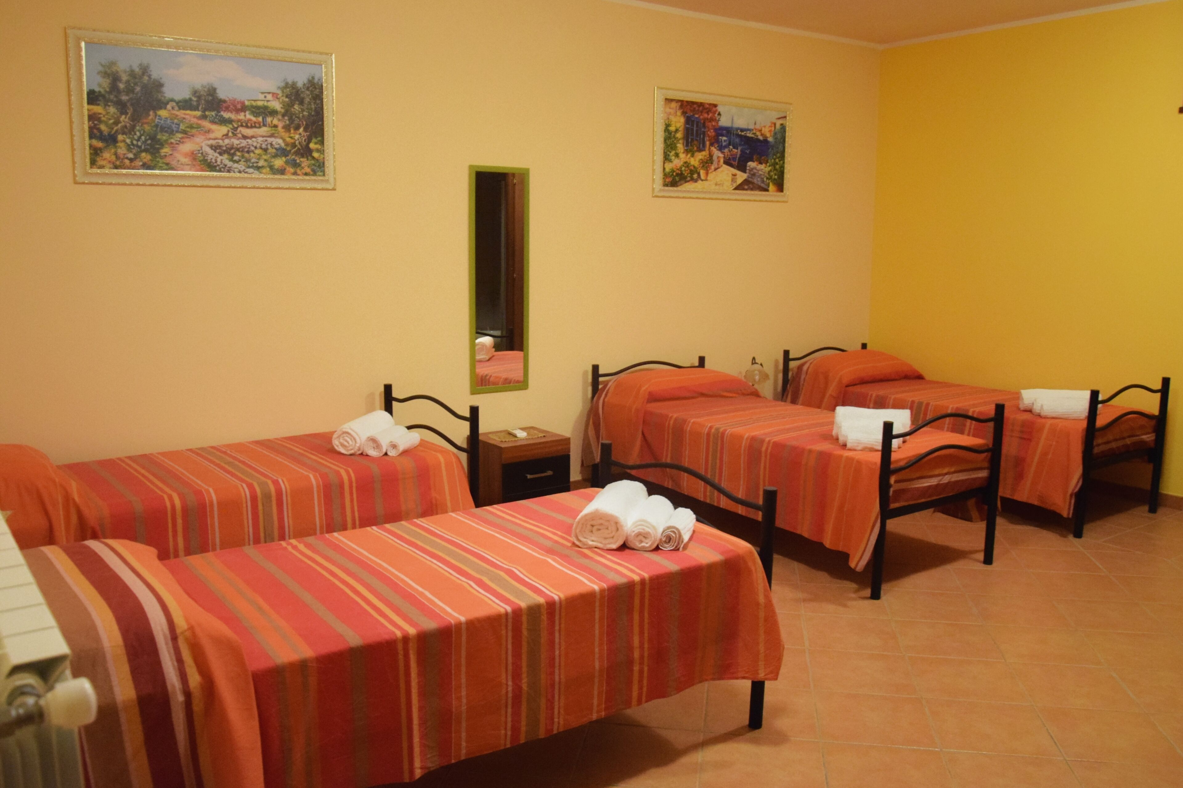 A hotel room with two single beds, a nightstand, a mirror, and two paintings on the walls.