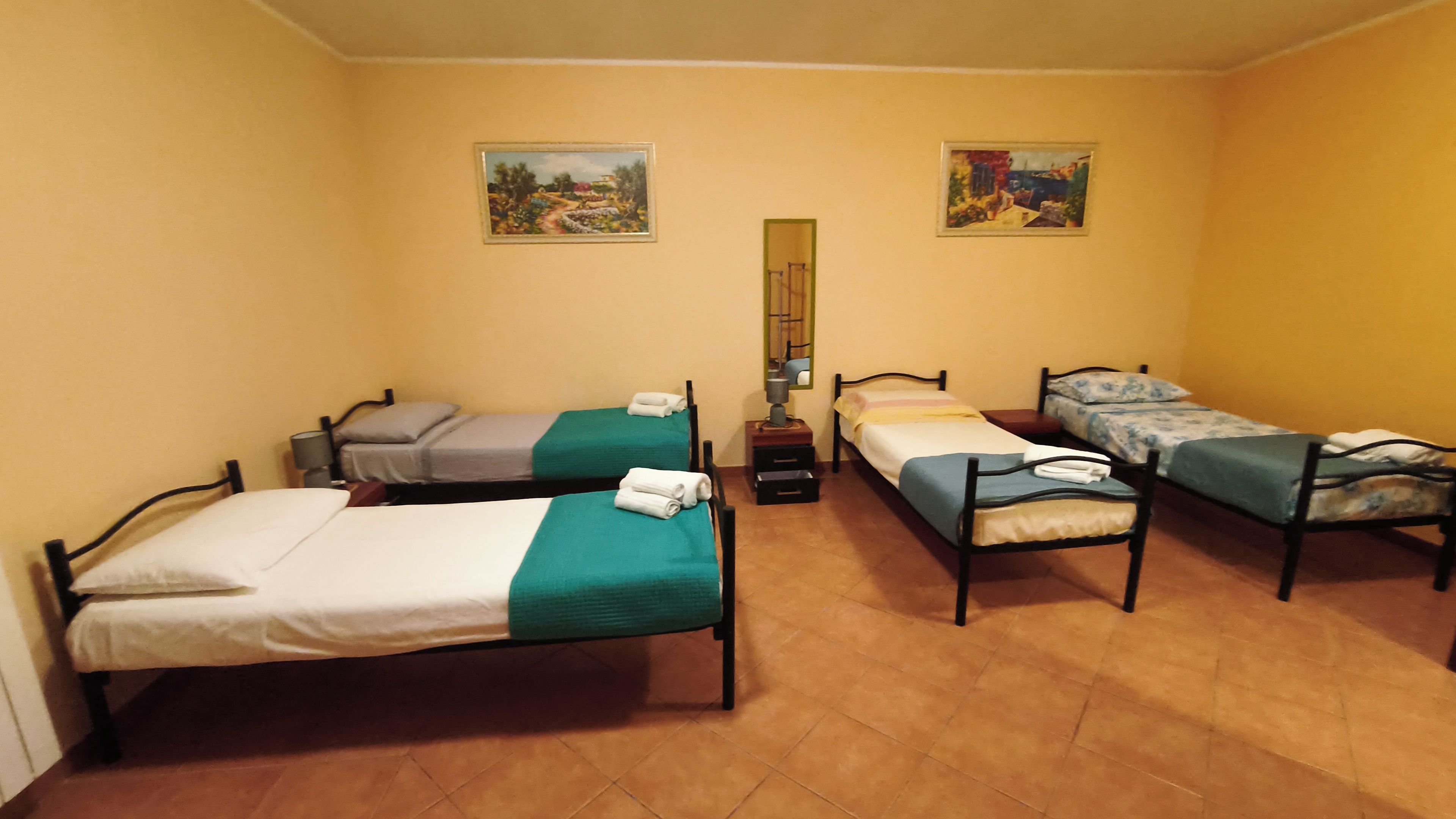 A room with four single beds, each with a green bedspread and white linens, arranged in a row.