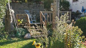 A garden with a wooden deck, a stone wall, and various plants and flowers. - ALL WOODEN APARTMENT WITH GARDEN 100 meters from town center in quiet location. (Gérardmer)
