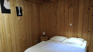 A wooden-paneled room with a bed, a nightstand, and a wall-mounted lamp. - ALL WOODEN APARTMENT WITH GARDEN 100 meters from town center in quiet location. (Gérardmer)