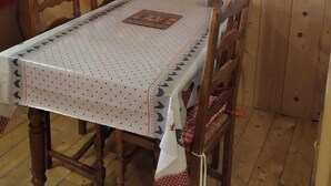 A wooden dining room with a table covered by a white tablecloth with black dots, surrounded by wooden chairs. - ALL WOODEN APARTMENT WITH GARDEN 100 meters from town center in quiet location. (Gérardmer)