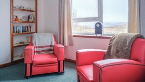Una stanza con una poltrona rossa, una libreria e una finestra vista campagna.