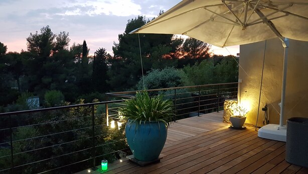 Eine Holzterrasse mit einem großen Kübelpflanzen, einer Tischlampe und Lichterketten.