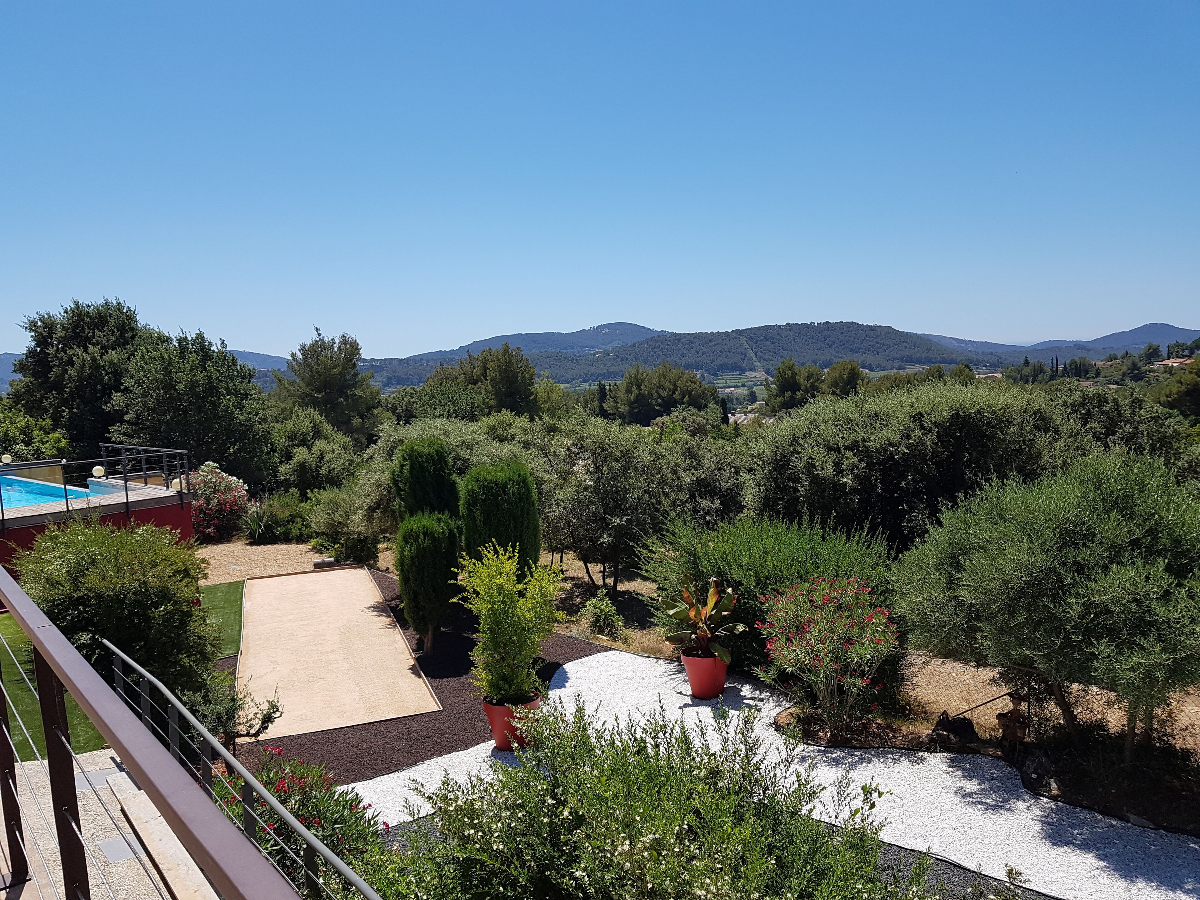Uma varanda com piscina, rodeada por vegetação exuberante e vista para colinas ao longe.