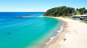 Una playa costera con aguas turquesas cristalinas, una orilla arenosa y un edificio con techo plano a la derecha.