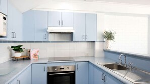 A modern kitchen with light blue cabinets, a stainless steel sink, and a built-in oven. - Breakers 2 - Beautiful bright apartment 50m to the sand (Mollymook)