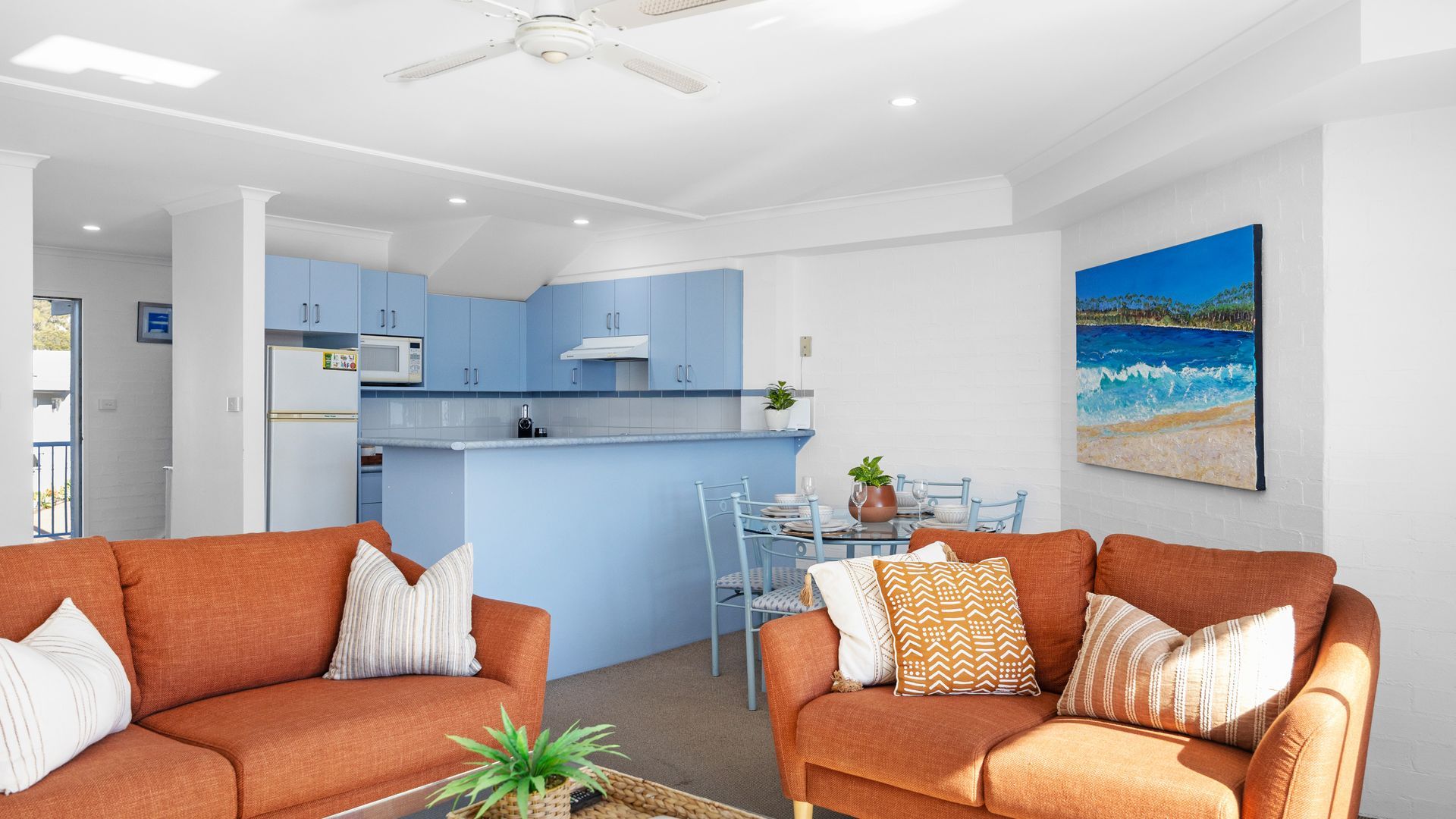 Ein modernes Wohnzimmer mit zwei Sofas, einem Essbereich mit Tisch und Stühlen sowie einer Küche mit blauen Schränken.