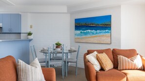 A dining area with a round table, chairs, and a painting of a beach scene.