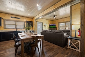 A wooden interior with a dining table set for four, a sofa, and a ceiling fan.