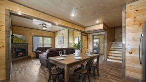 Accogliente interno in legno con camino, tavolo da pranzo per quattro persone e una scala che conduce a un altro livello.