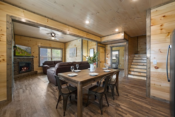 A cozy wooden interior with a fireplace, a dining table set for four, and a staircase leading to another level.