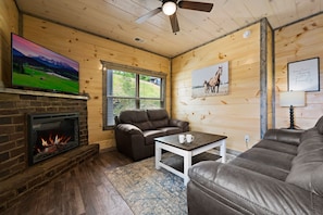 A cozy living room with a fireplace, leather sofas, a television, and artwork on the walls.