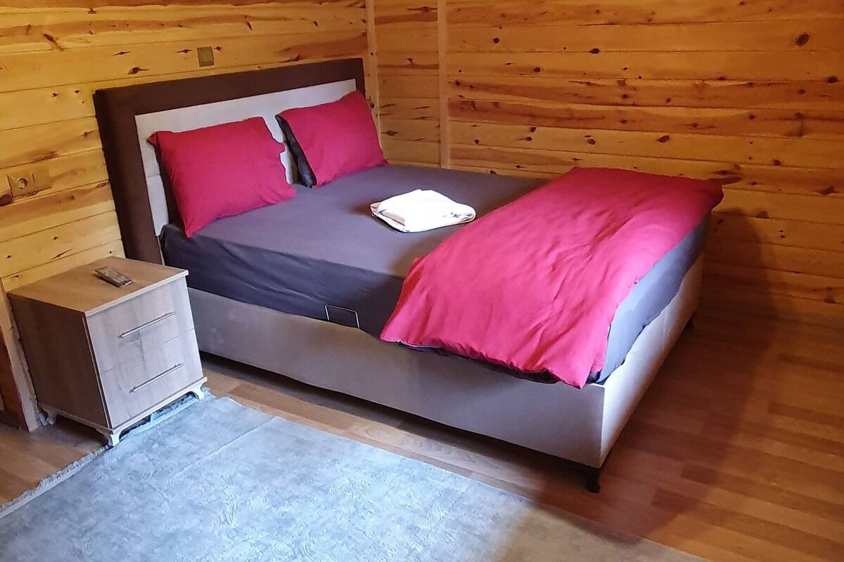 A wooden cabin bedroom with a bed, a nightstand, and a hanging light fixture.