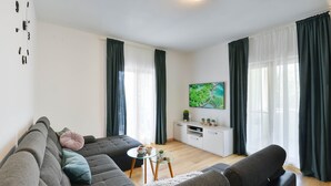 Een moderne woonkamer met een hoekbank, een glazen salontafel en een witte televisiemeubel met een flatscreen-televisie.
