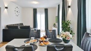 Een moderne eetruimte met een ontbijt aan tafel, een bank achtergrond en een wandklok.