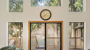 Une pièce dotée d’une grande porte-fenêtre coulissante donnant sur une terrasse extérieure avec une rambarde en bois, une horloge au mur et un fauteuil vert agrémenté d’un coussin.