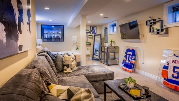 A modern living room with a grey sectional sofa, a coffee table with a plant, and a sports jersey on display. - Luxury Studio Suite. Walking distance to UBS Arena (Elmont)