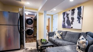 A modern living room with a grey sofa, a coffee table, and a large abstract painting on the wall. - Luxury Studio Suite. Walking distance to UBS Arena (Elmont)