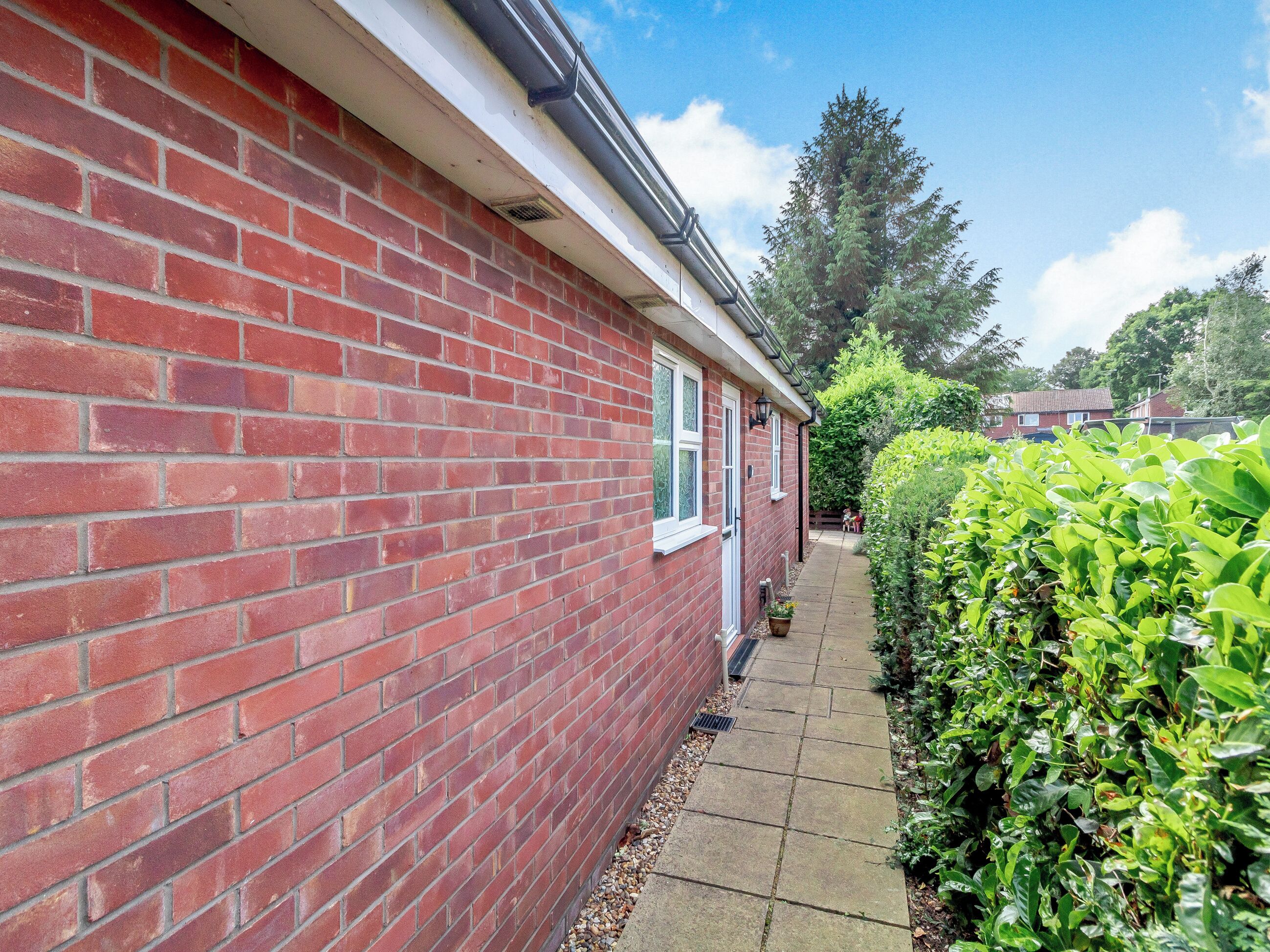 A red brick house with a white window frame, a door, and a small garden area with a hedge and a pathway.