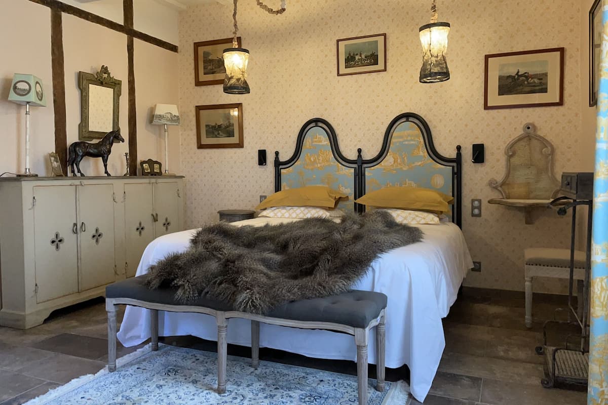 A bedroom with a bed, a bench, a wardrobe, and a chandelier.