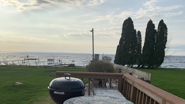 A deck with a grill and a table, overlooking a body of water and trees.