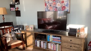A living room with a TV, wooden furniture, a bookshelf, and a floral painting on the wall.