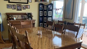 A dining room with a large wooden table, chairs, a chandelier, and framed family photos on the walls.