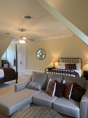 A cozy bedroom with a bed, a gray sectional sofa, a wooden coffee table, and a ceiling fan. - Private oasis, fully furnished, ready to move in. Luxury finishes.  6beds 7baths (Biloxi)