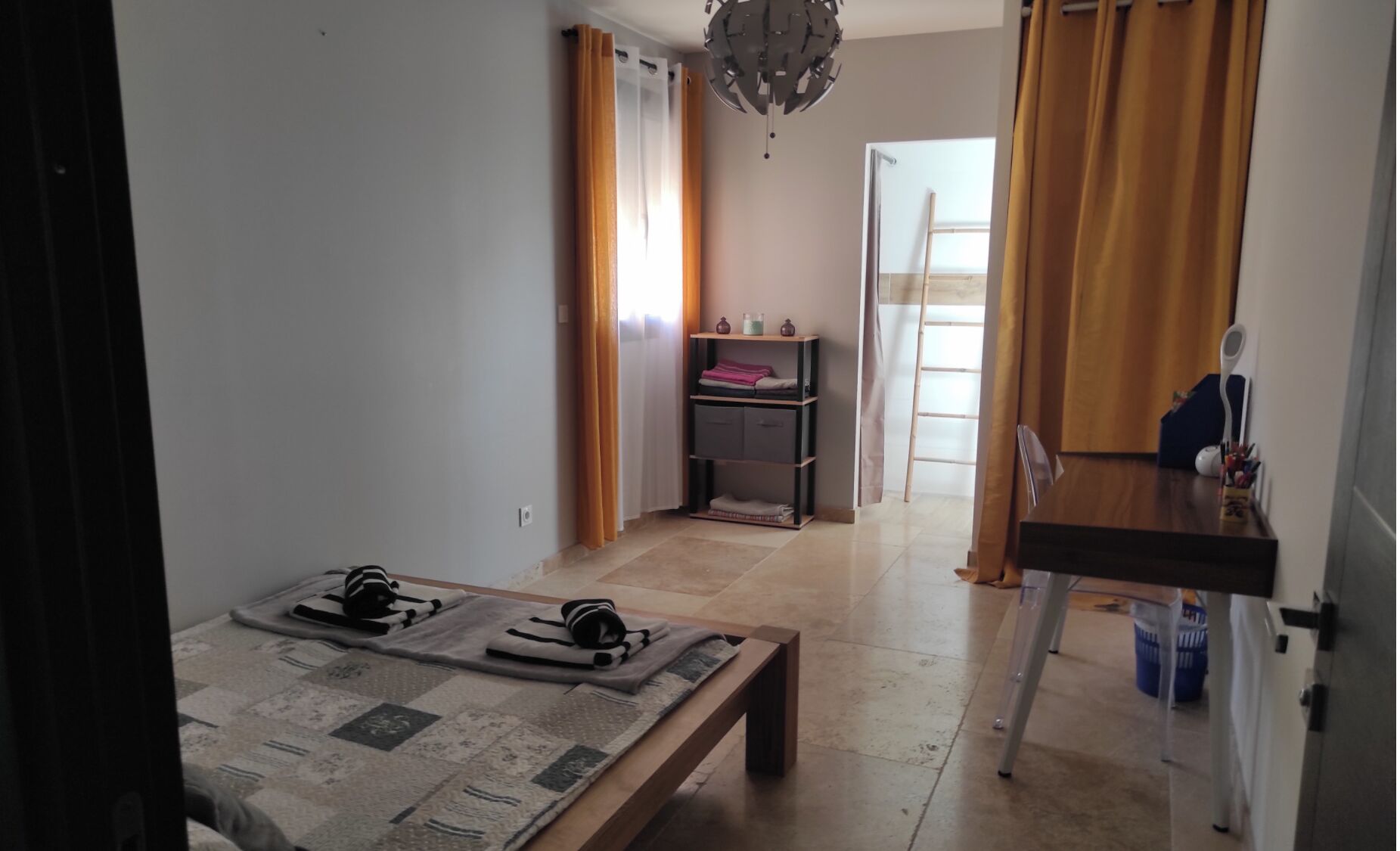 Una habitación con cama, escritorio, silla, ventana con cortinas y puerta.