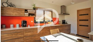 A modern kitchen with wooden cabinets, a dining table, and a window with blinds. - Beautiful villa near Uzès (Blauzac)