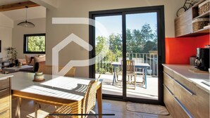 A modern kitchen with a dining area, large sliding glass doors to an outdoor patio, and a TV mounted on the wall. - Beautiful villa near Uzès (Blauzac)