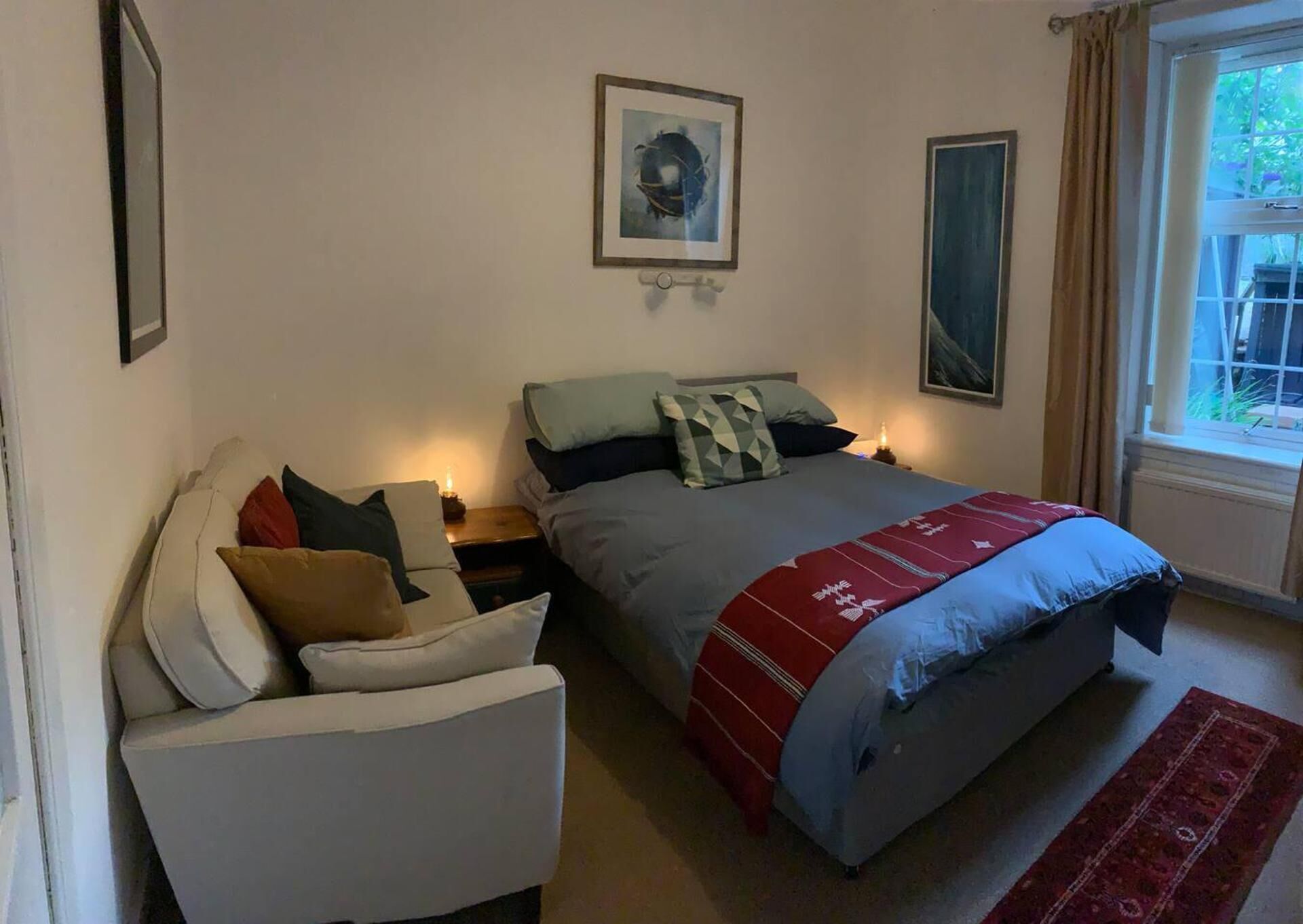 A bedroom with a bed, a chair, a nightstand, a window, and a framed picture on the wall.