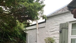 A gravel path leading to a white building with a green door and window shutters. There are potted plants along the path and a black fence on one side. - Cedarbank's - The Little Art House - dog Friendly (Dunoon)