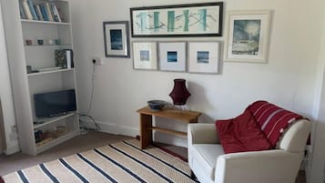 A living room with a white armchair, a striped rug, a bookshelf, and framed artwork on the wall.