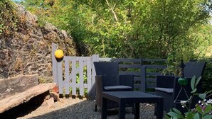 An outdoor seating area with a wooden table and chairs, surrounded by a wooden fence and greenery. - Cedarbank's - The Little Art House - dog Friendly (Dunoon)