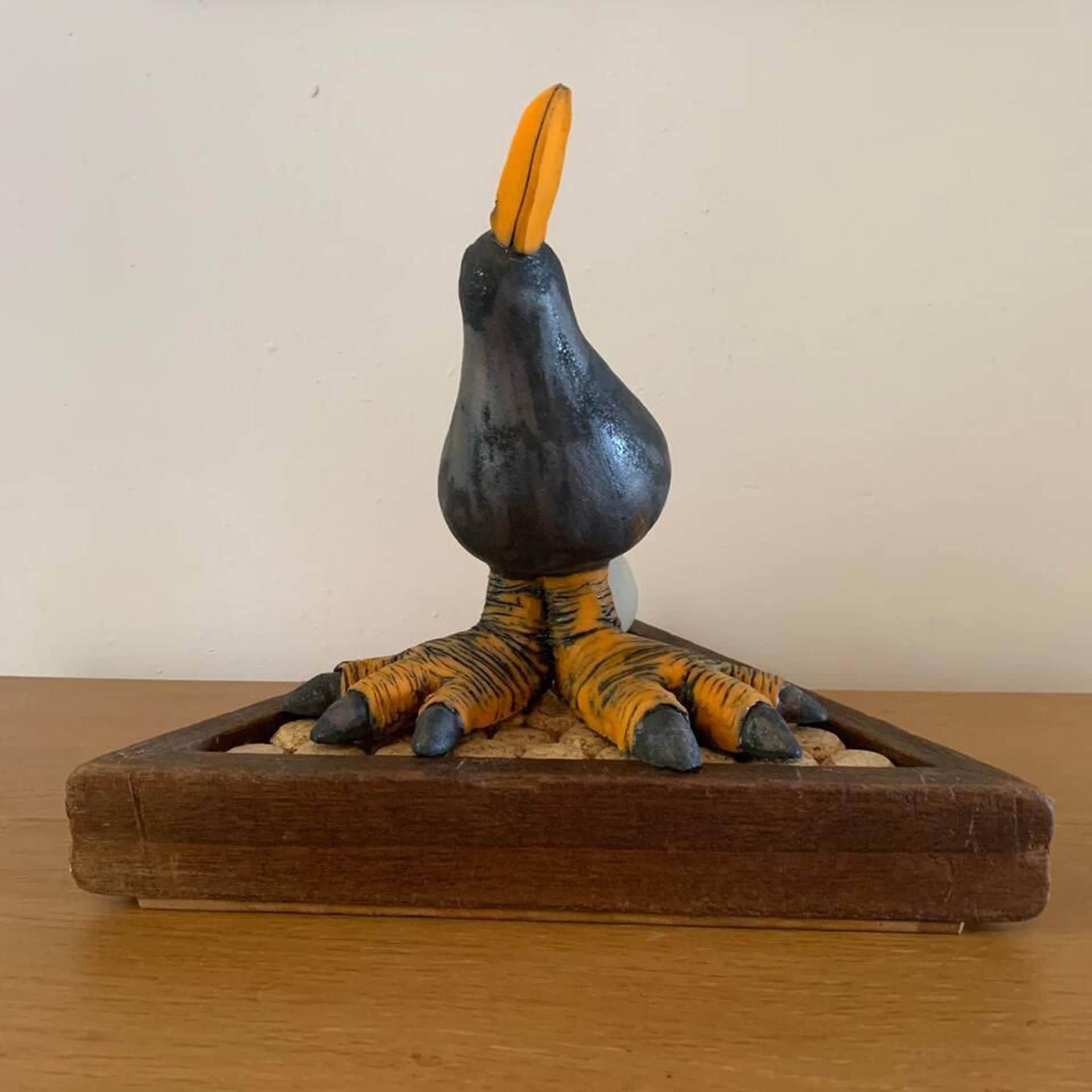 A sculpture of a bird with a curved beak, resting on a wooden base.